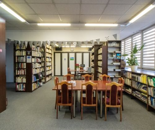 wnętrze biblioteki, regały z książkami, czasopismami, stół z krzesłami