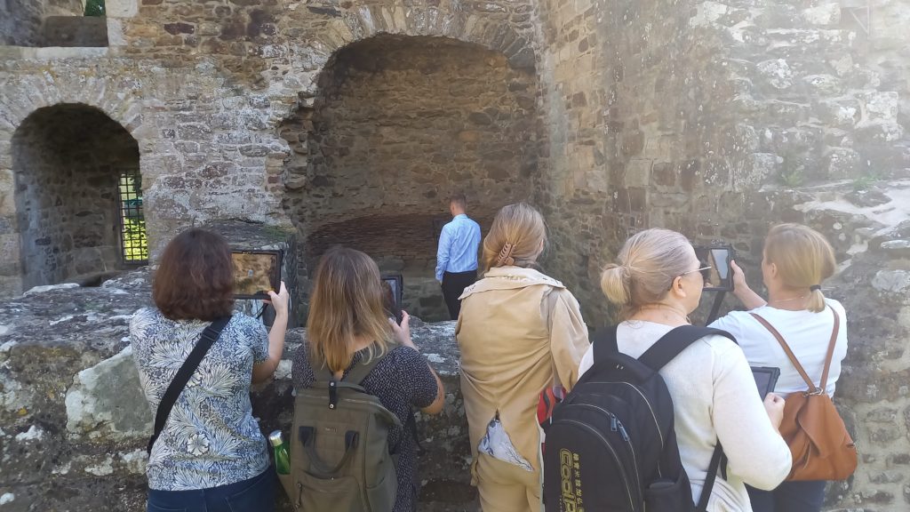 kilka osób stoi z tabletami przed murami zamku
