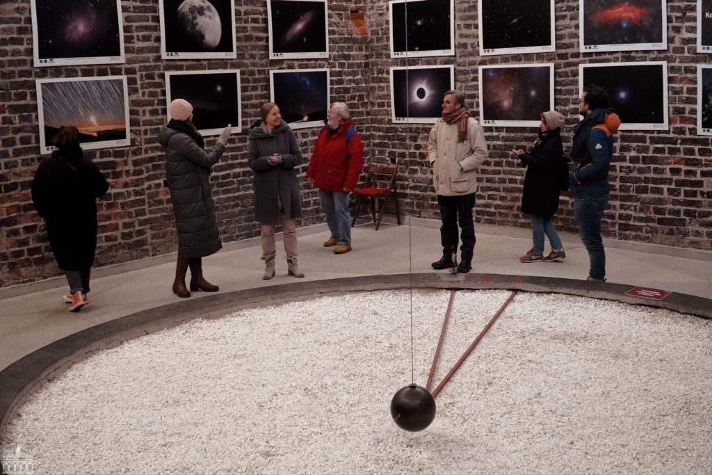 grupa ludzi stoi we wnętrzu muzeum, na ścianach wiszą plansze dotyczące układu planetarnego