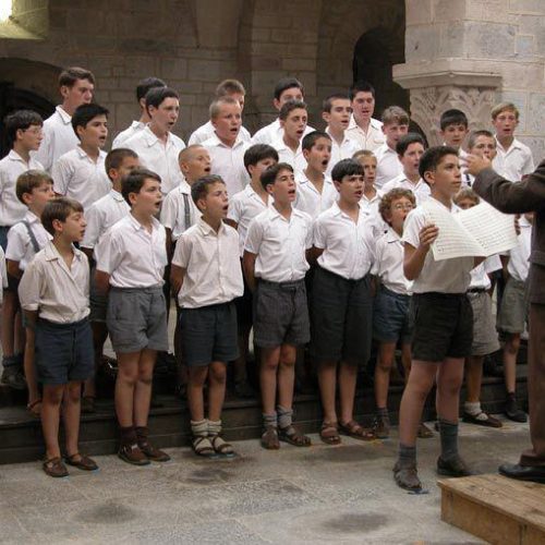 kadr z filmu les choristes. dzieci w chórze, białe koszulki i ciemne spodenki, przed nimi nauczyciel w garniturze stojący na podwyższeniu